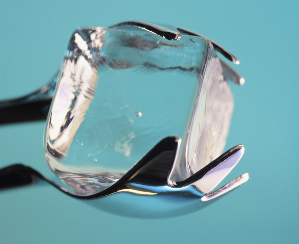 Square ice cube held with tongs