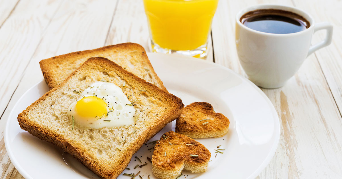 Egg fried in a heart-shaped toast cutout sprinkled with cracked pepper and rosemary, orange juice and cup of espresso. Wooden table. Selective focus