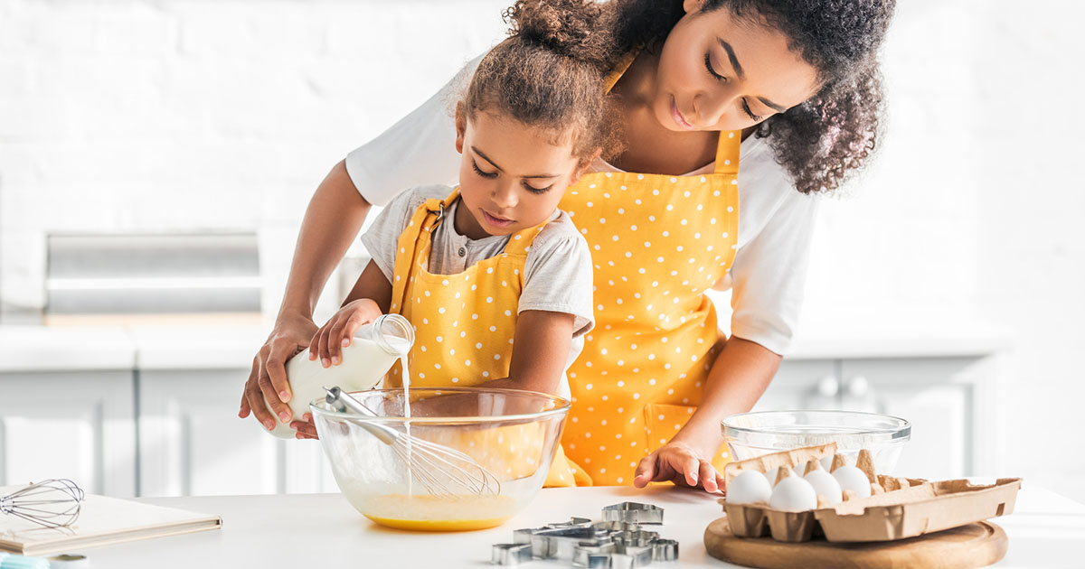 mother and daughter preparing dough and pouring milk into bowl