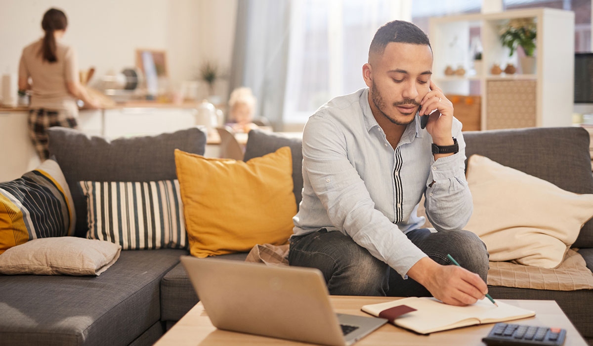 Man working from home, family in the kitchen behind him